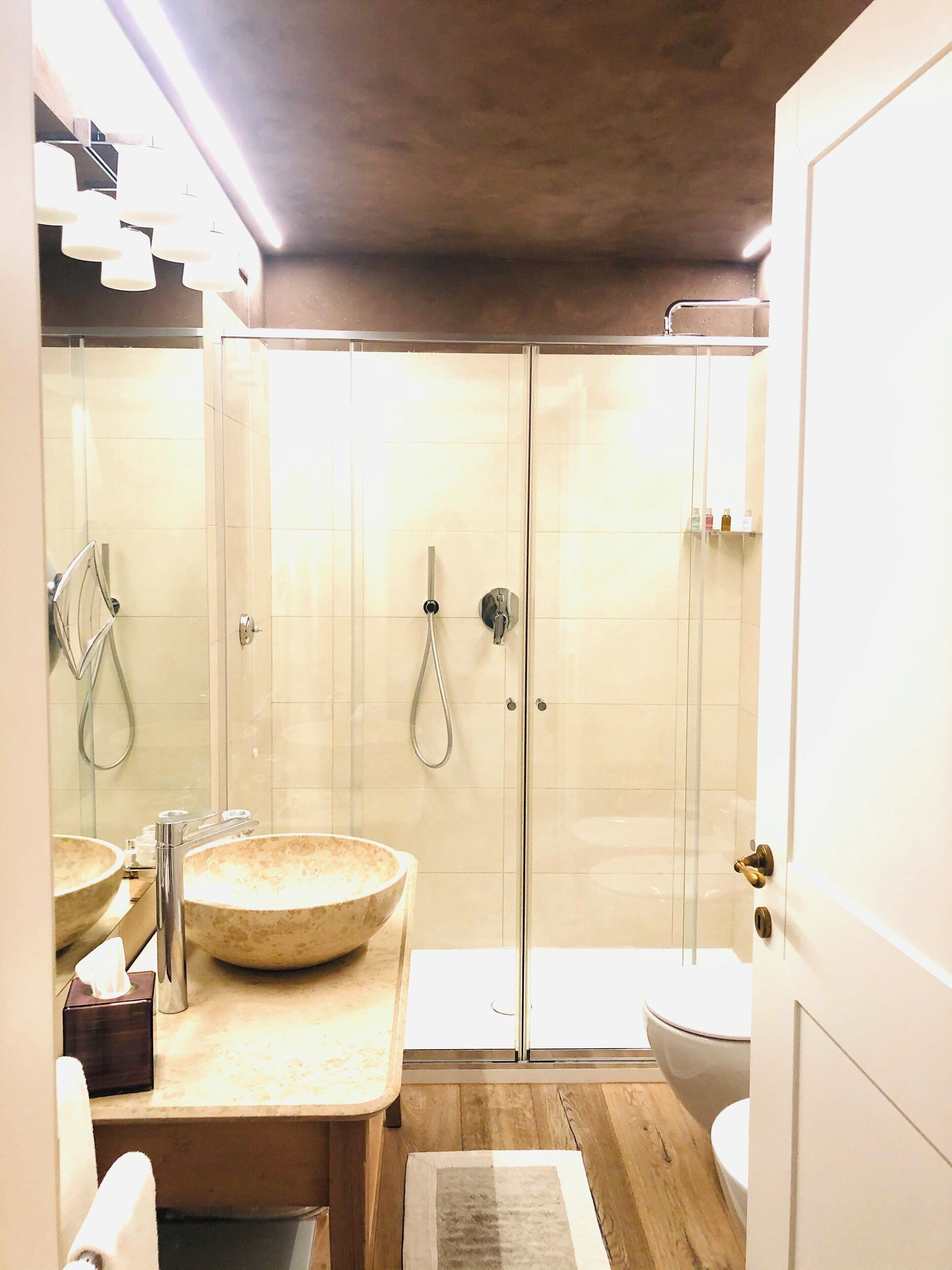 A bathroom with a glass-enclosed shower, a wooden vanity with a large bowl sink, and a toilet.