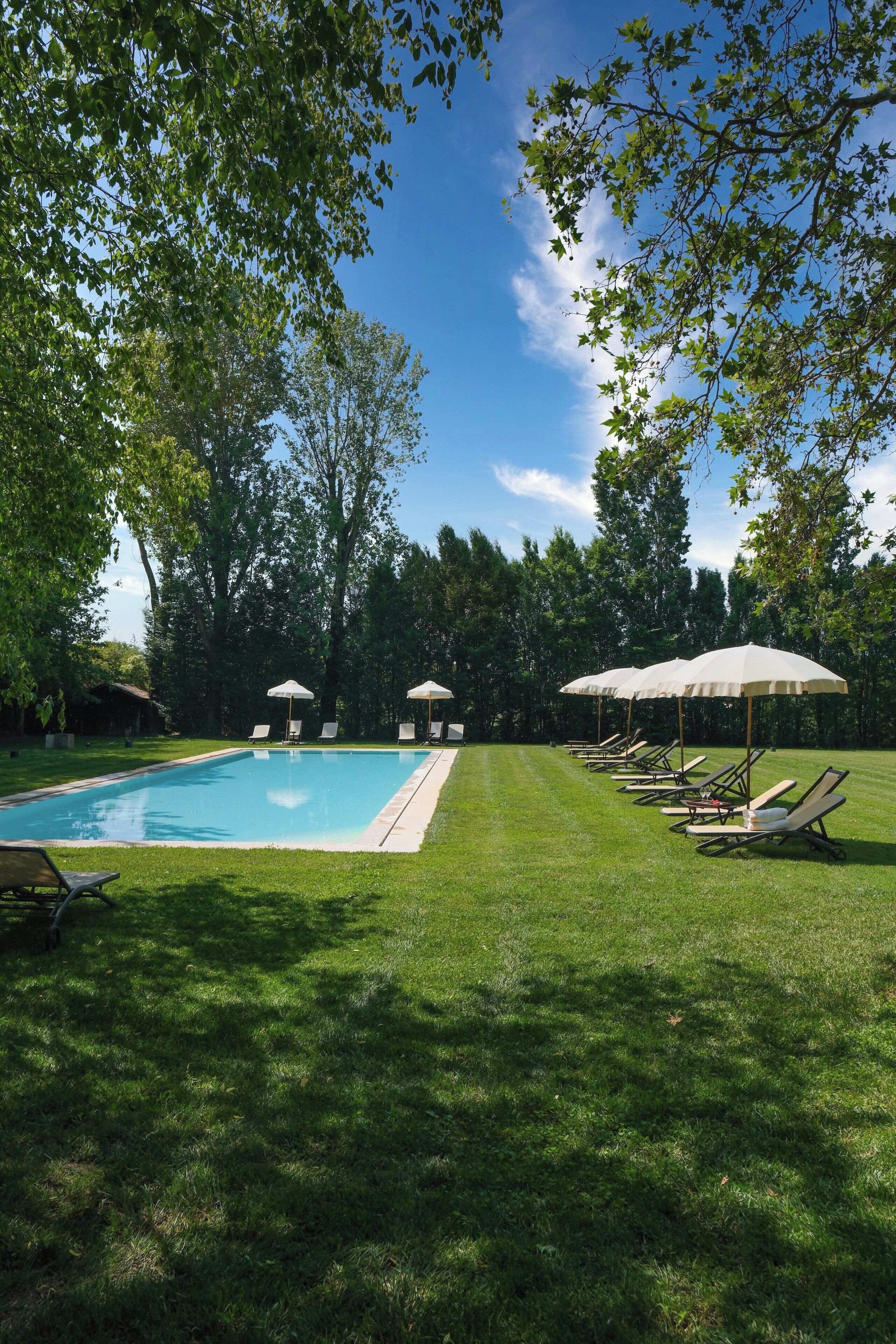 Una piscina amb gandules i ombrelles, envoltada d'arbres.