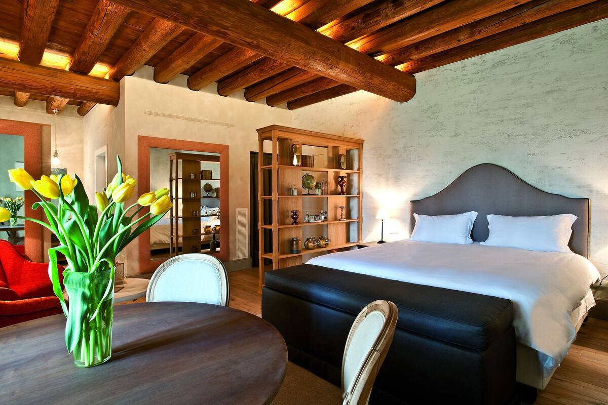 Un dormitorio con una cama grande, una estantería de madera, una mesa de comedor con sillas y un jarrón de tulipanes.