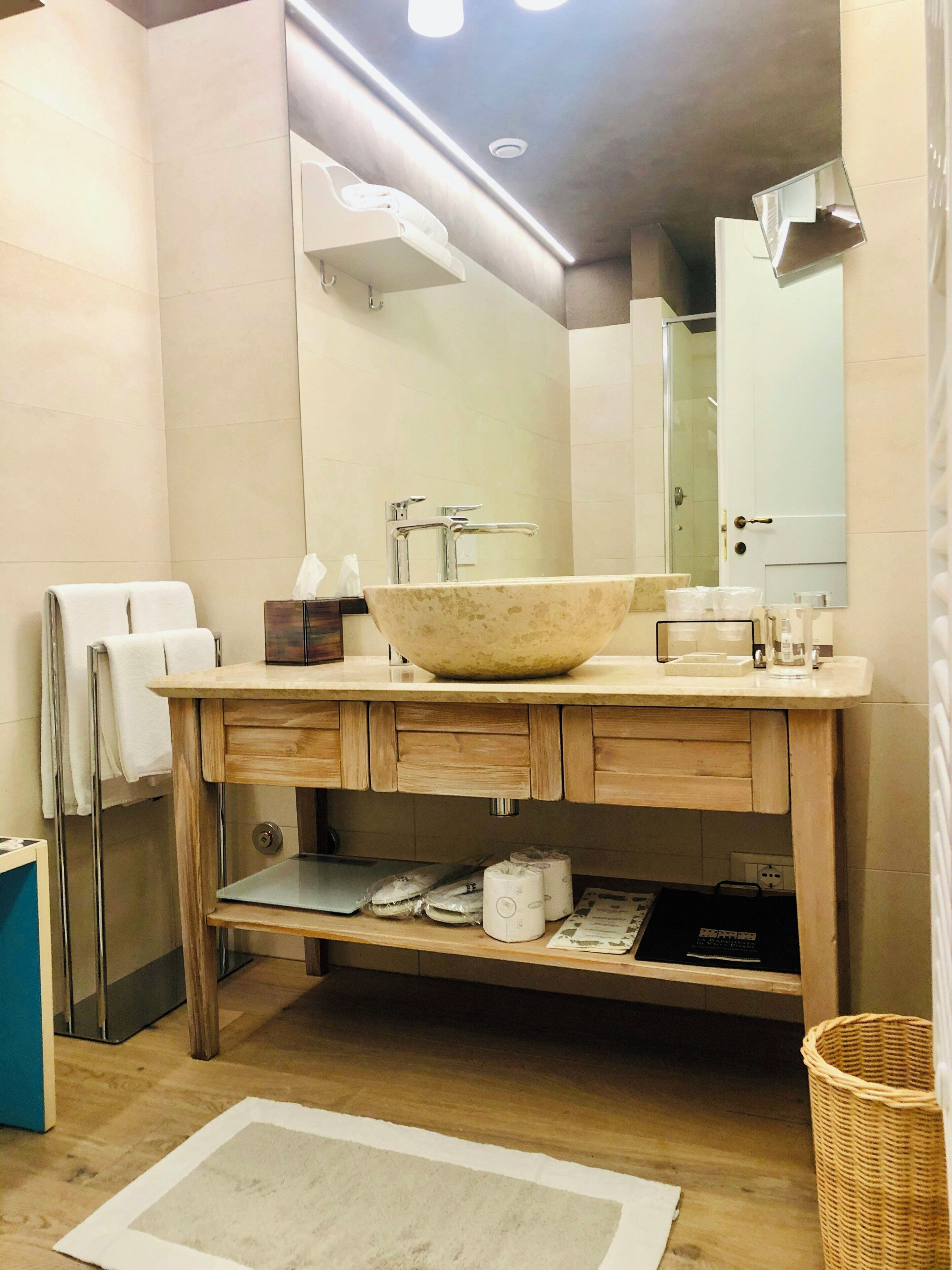 A bathroom with a large bowl sink, wooden vanity, mirror, and a small rug on the floor.