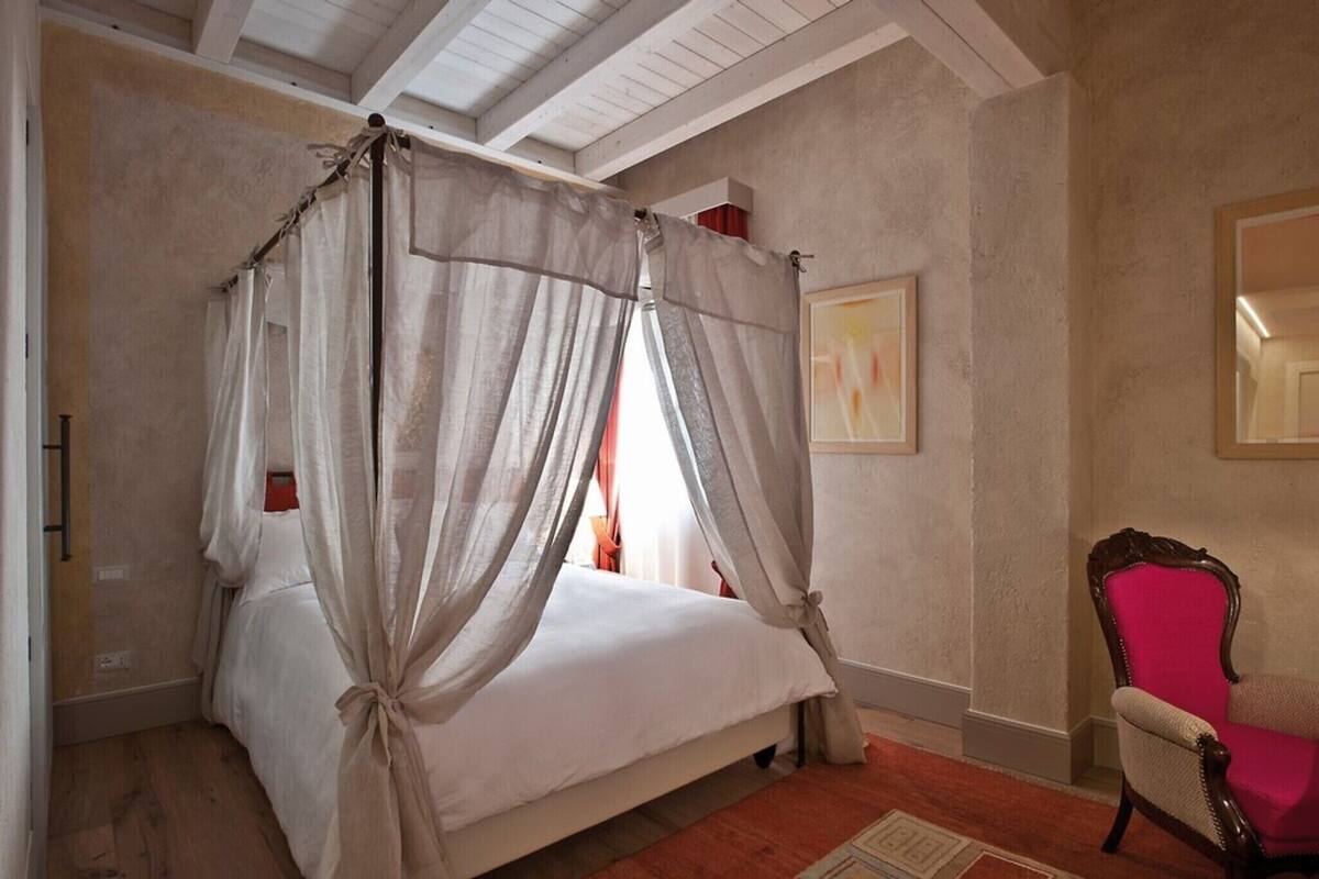 Un dormitorio con cama con dosel, una silla y un cuadro en la pared.