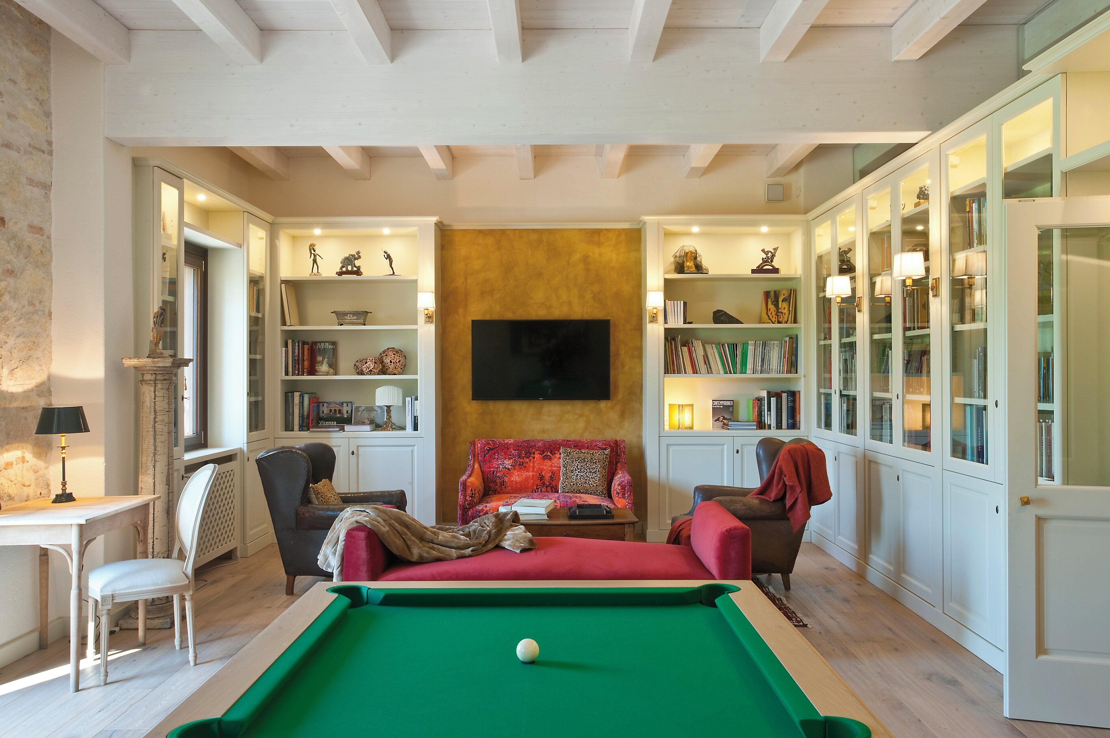 Un salon chaleureux avec une table de billard, un canapé, un fauteuil et des étagères intégrées.