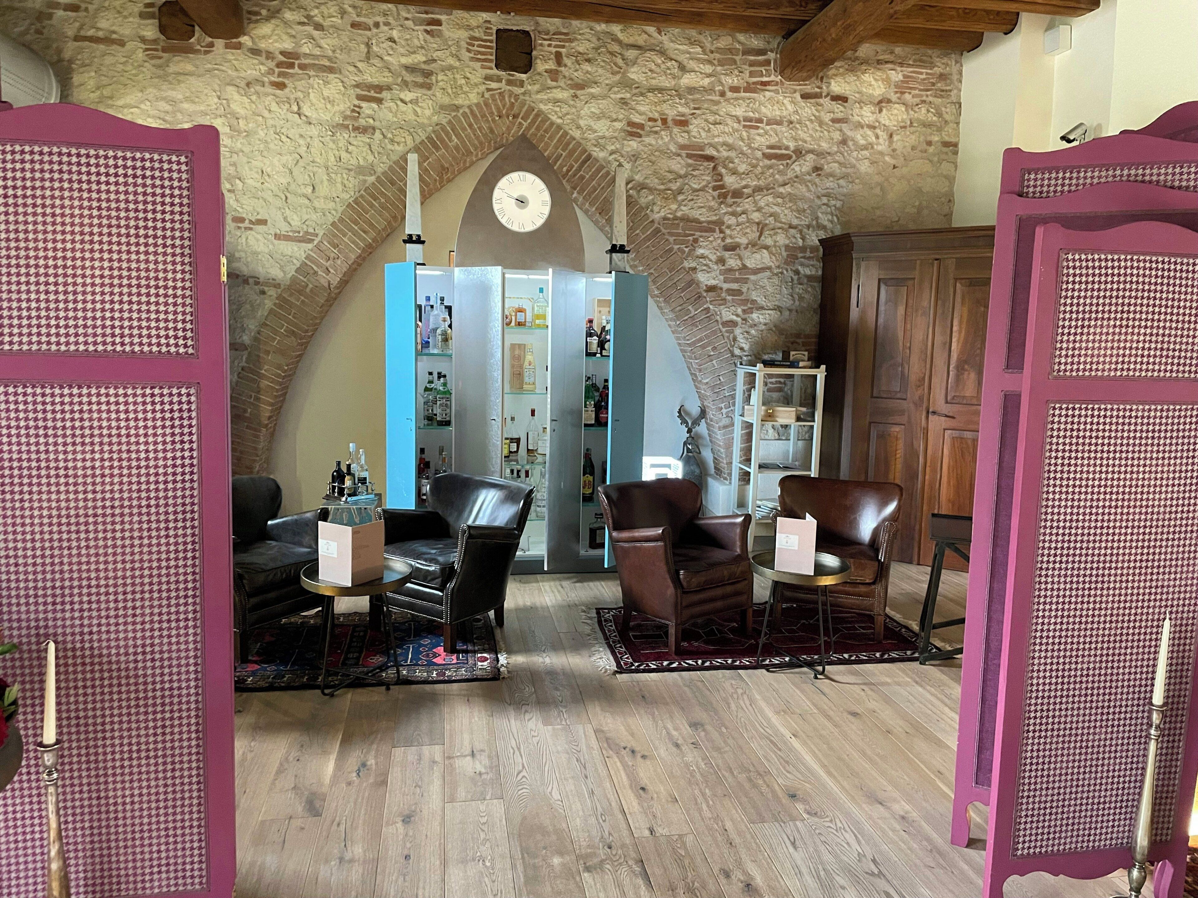 Une pièce avec un mur en pierre, une horloge, des fauteuils en cuir, une petite table et une bibliothèque.