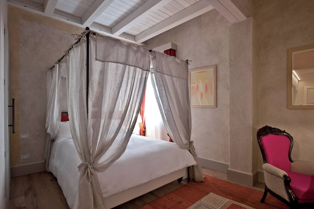 Un dormitorio con una cama con dosel, una silla y un cuadro en la pared.