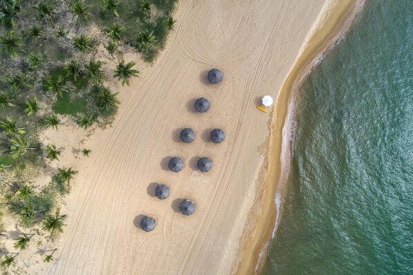 Vue aérienne d’une plage avec plusieurs parasols et une chaise longue blanche.