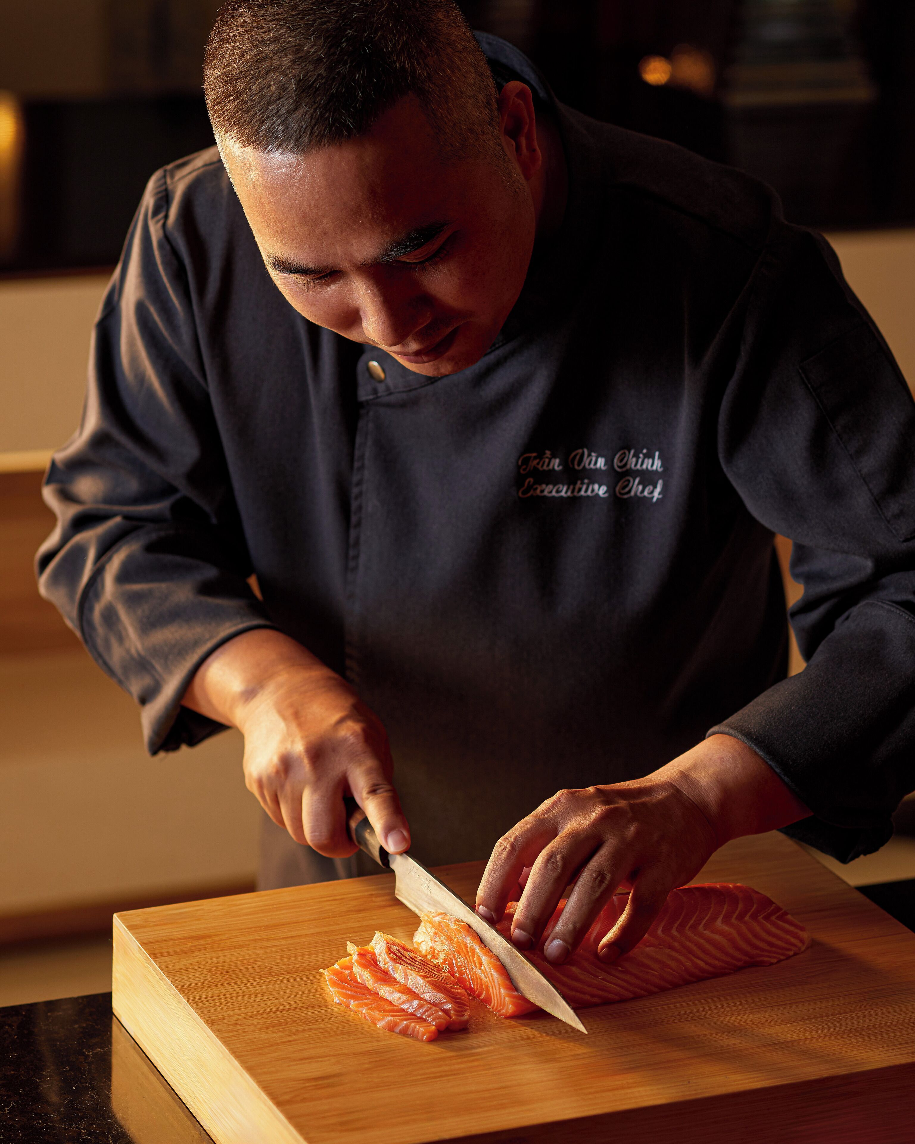 A chef slicing salmon on a wooden cutting board.