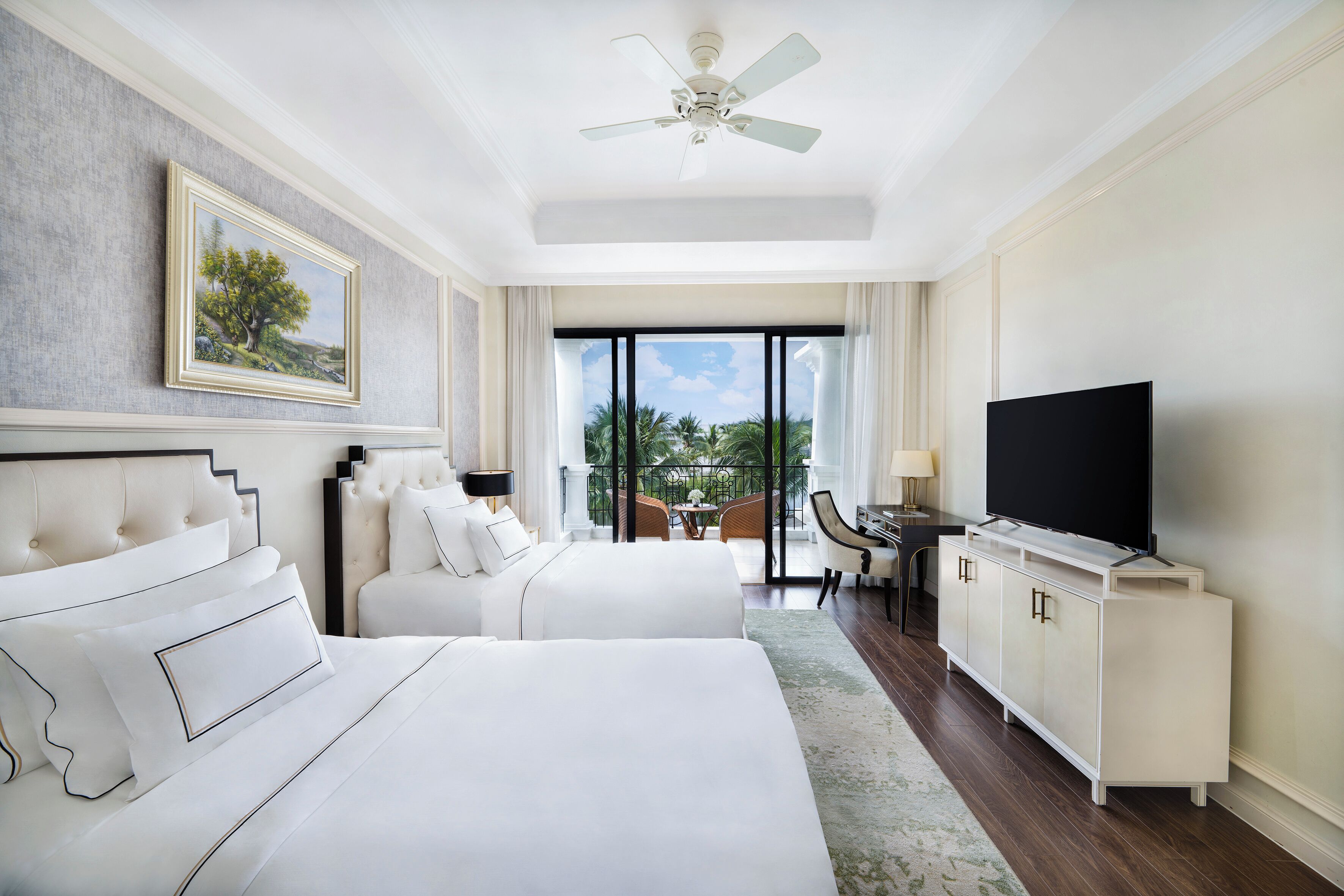A hotel room with a large bed, a television, a desk, and a balcony with a view of palm trees.