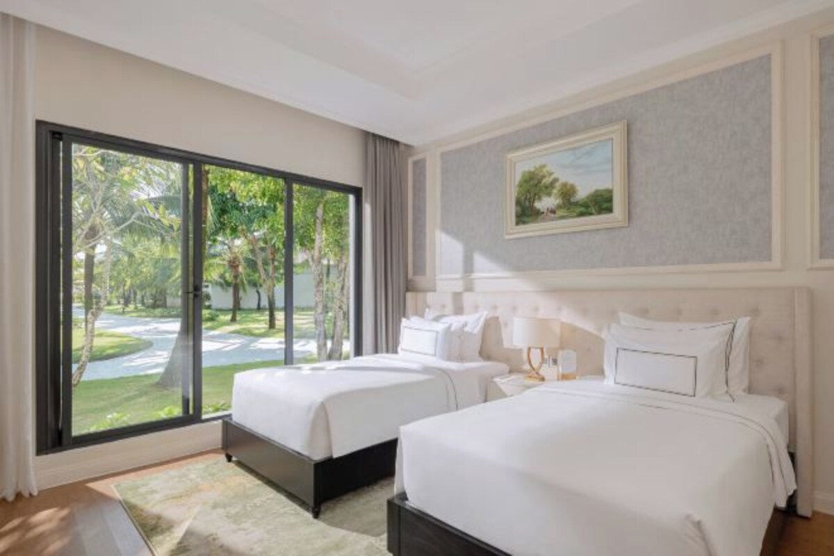 Hotelkamer met twee bedden, een groot raam met uitzicht op groen, een schilderij aan de wand en een lichtkleurig vloerkleed.