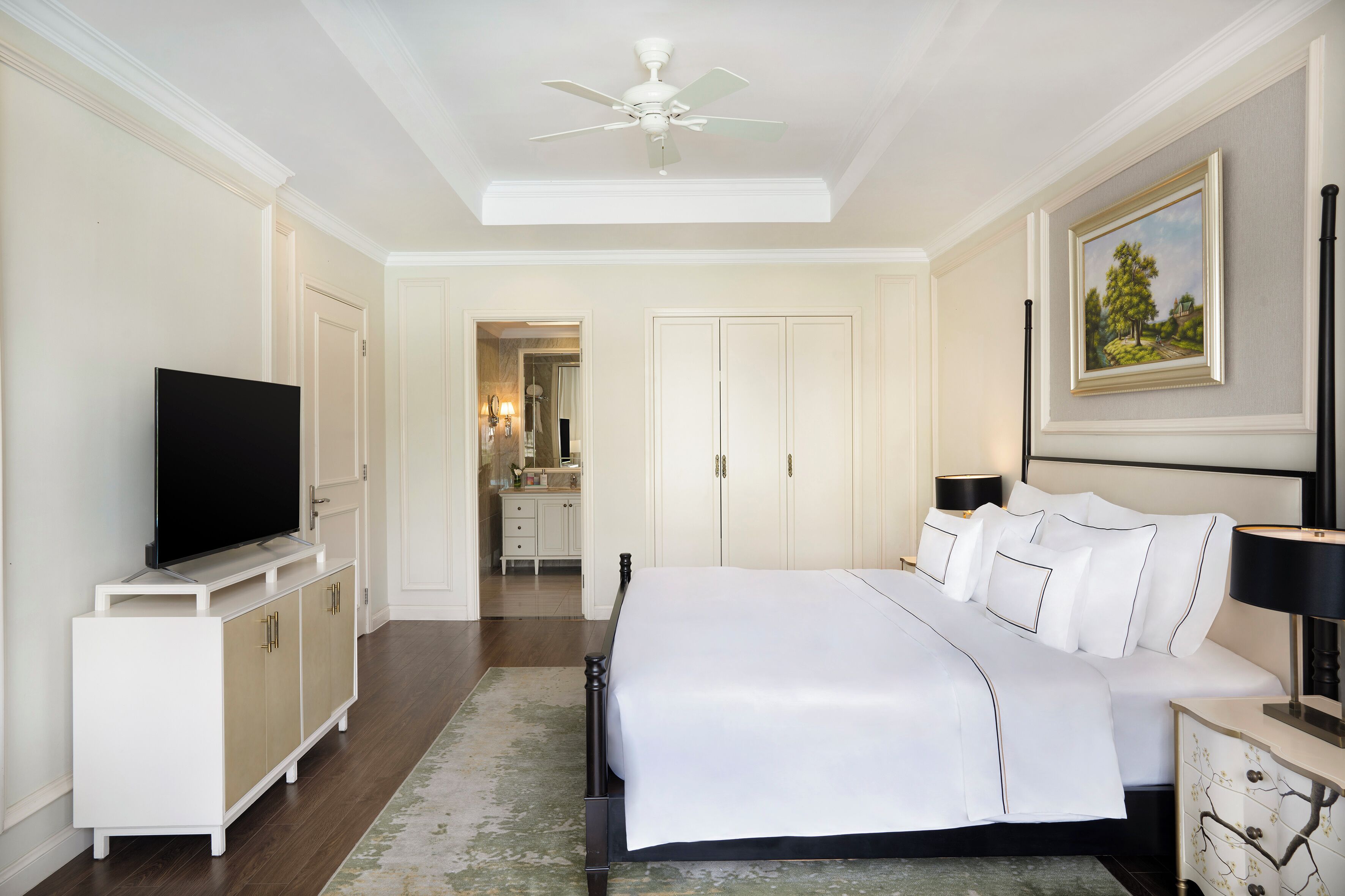 A hotel bedroom with a bed, television, wardrobe, and a painting on the wall.