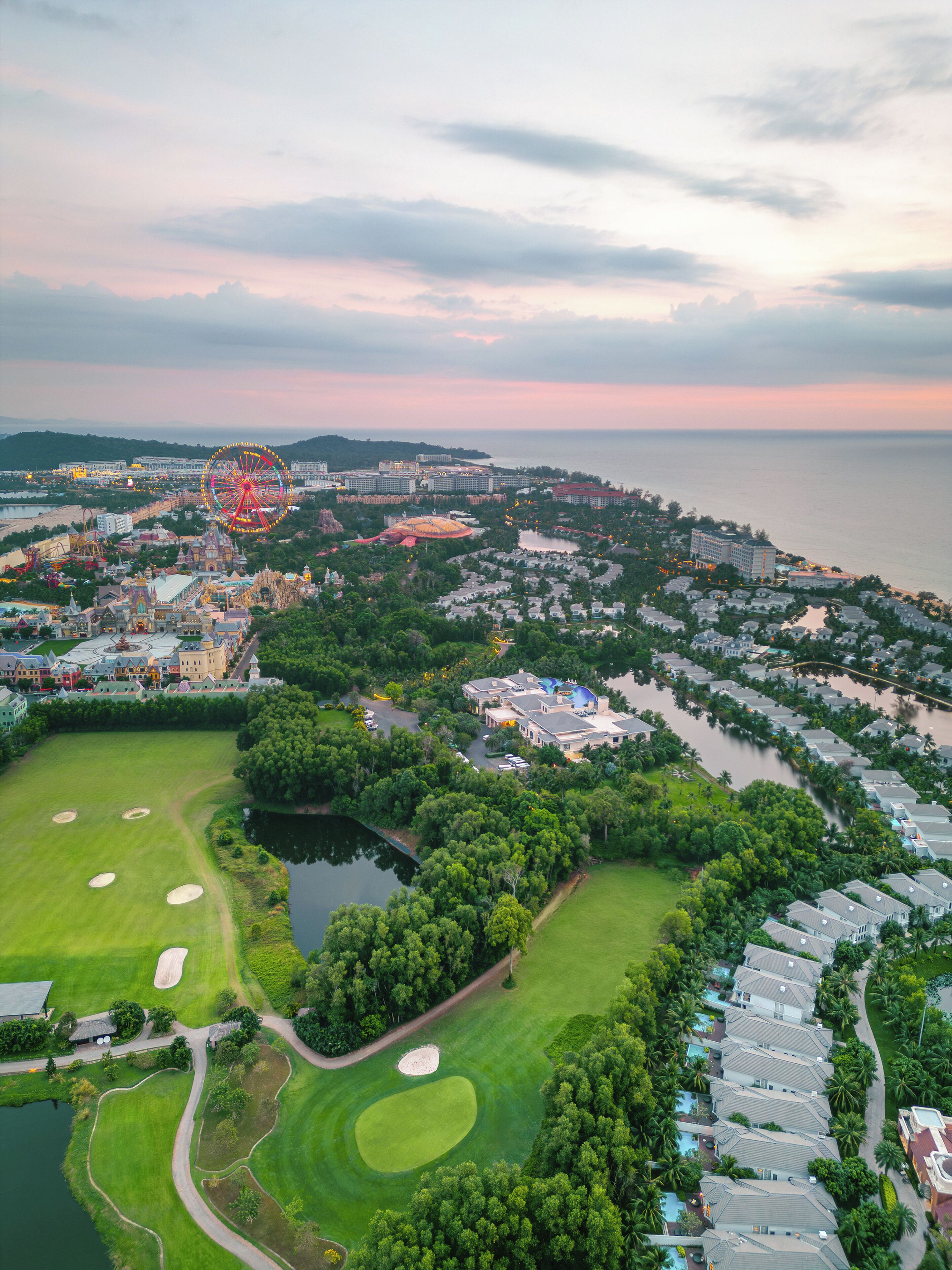 An aerial view of a coastal resort area with a large Ferris wheel, a golf course, and a marina.