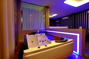 A modern spa room with a large bathtub, a reception desk, and a window with curtains.