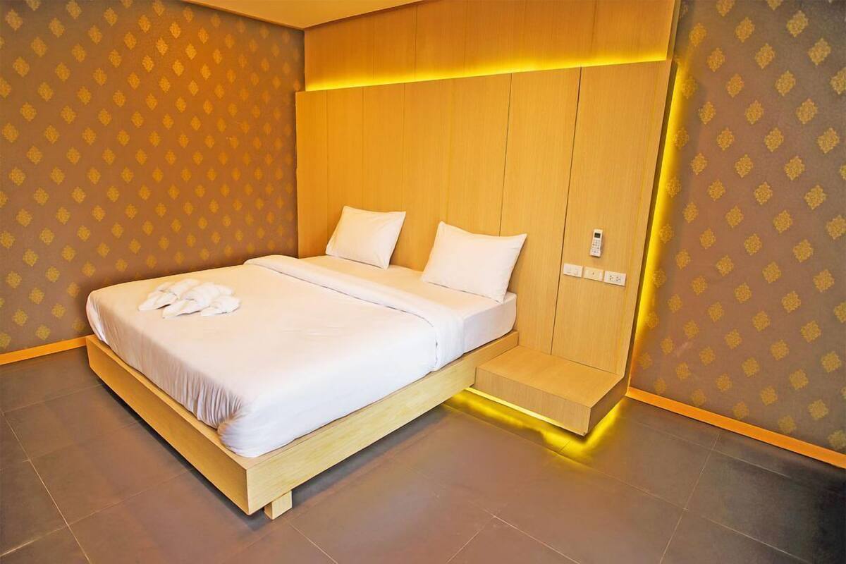 Una habitación de hotel moderna con estructura de cama de madera, ropa de cama blanca y un banco incorporado al pie de la cama.