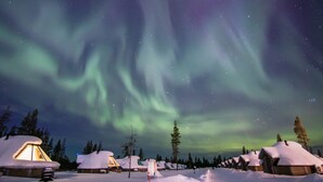 En rad snötäckta stugor med utsikt över norrskenet.