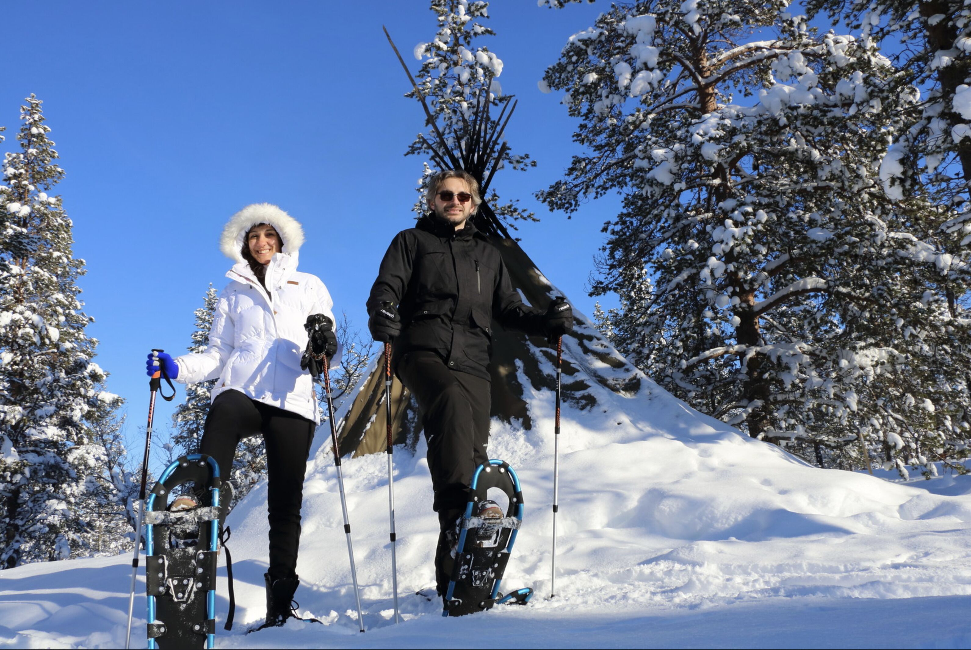 Zwei Personen mit Schneeschuhen in einer verschneiten Landschaft mit Bäumen.