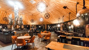 En restaurang med träpanel i tak och på väggarna, runda bord och orange stolar.