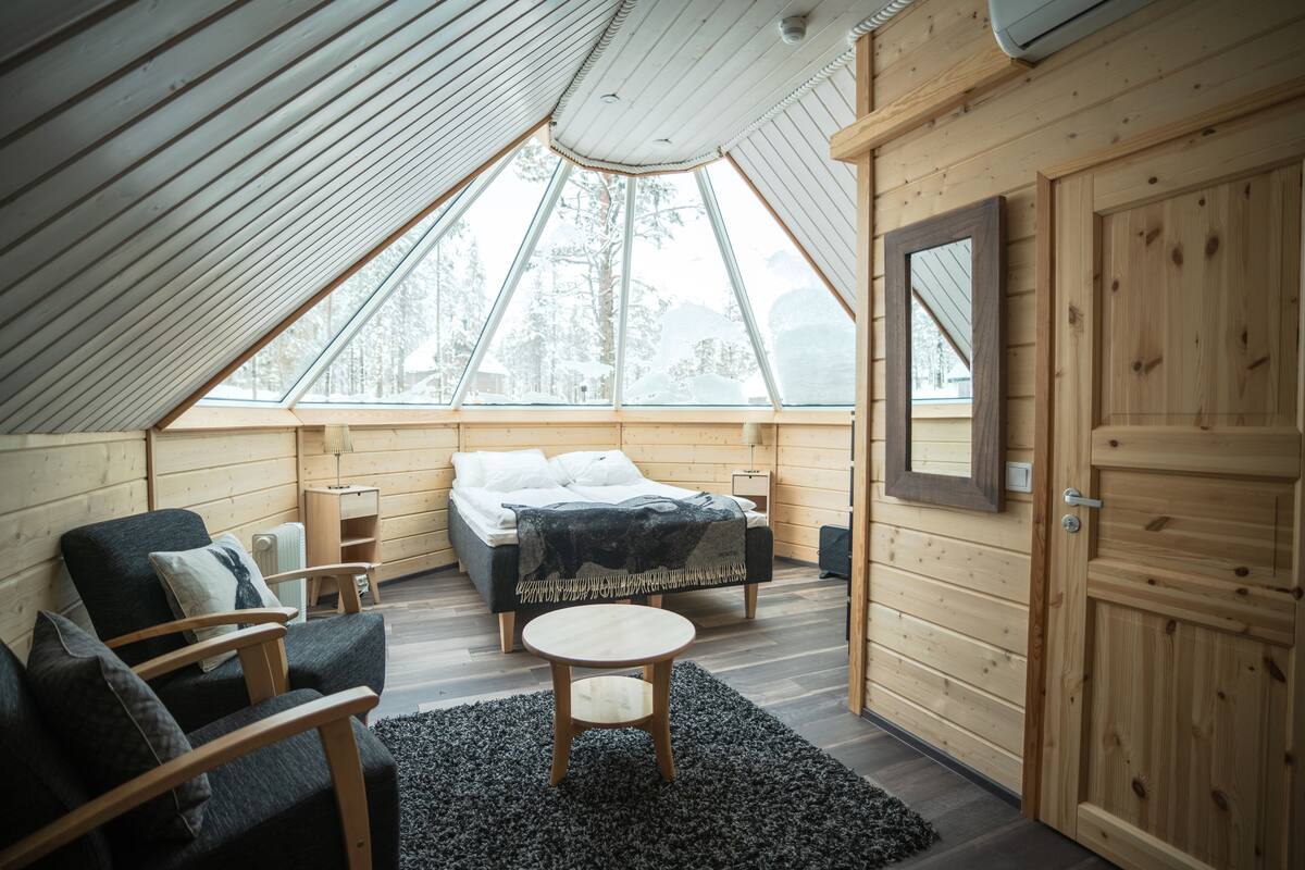 Ein gemütliches Schlafzimmer im Dachgeschoss mit schrägen Wänden, einem Bett, einem Sessel, einem kleinen Tisch und einer Tür.