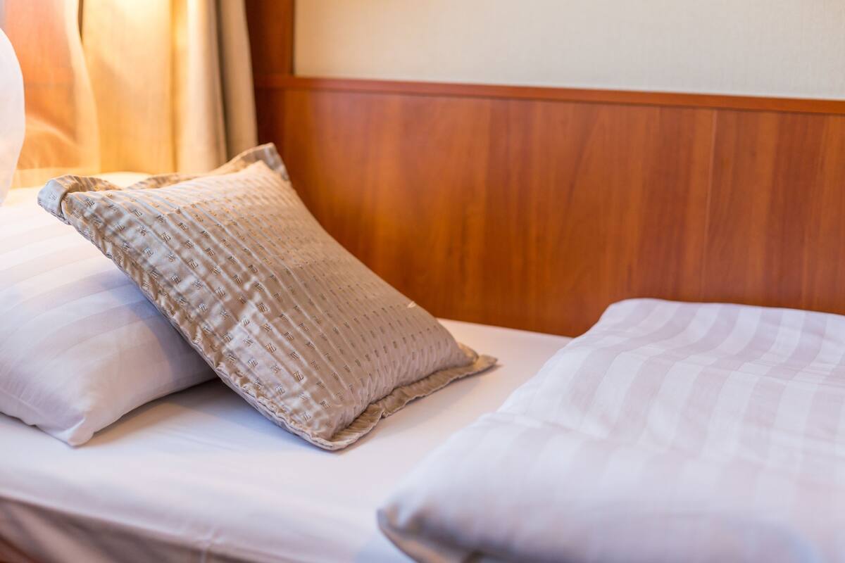 A neatly made bed with white linens and a patterned pillow.