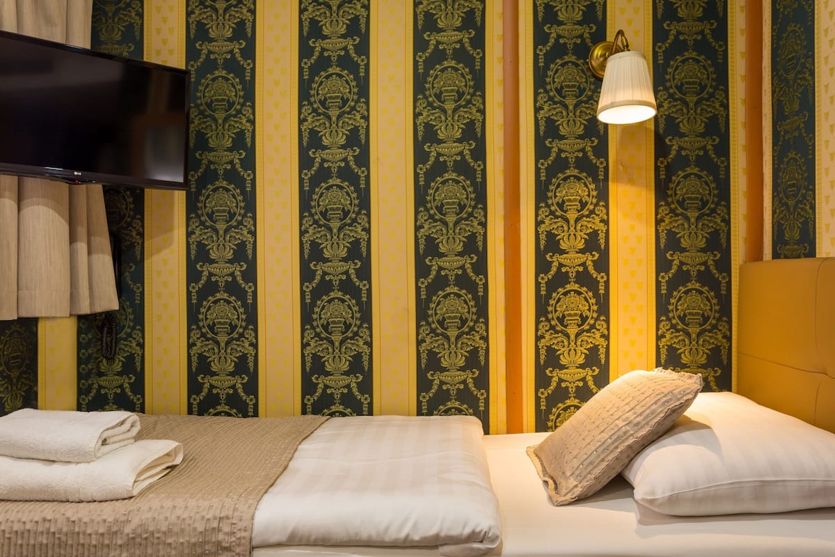 A hotel room with two beds, a flat-screen TV, and a wall with vertical patterned wallpaper.