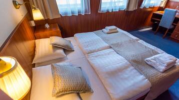 A double bed with two pillows, a bedside table with a lamp, and a small desk with a chair.