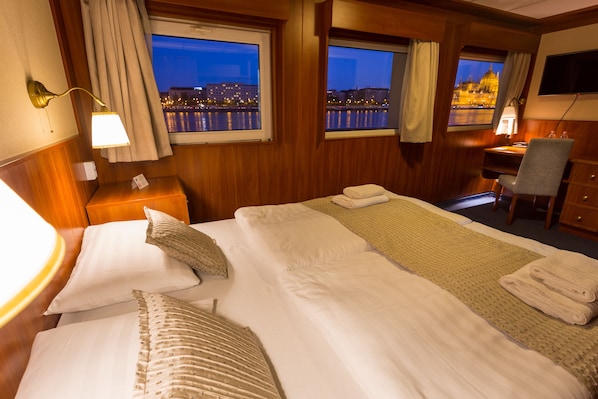 A hotel room with two beds, a desk, a chair, and a TV.