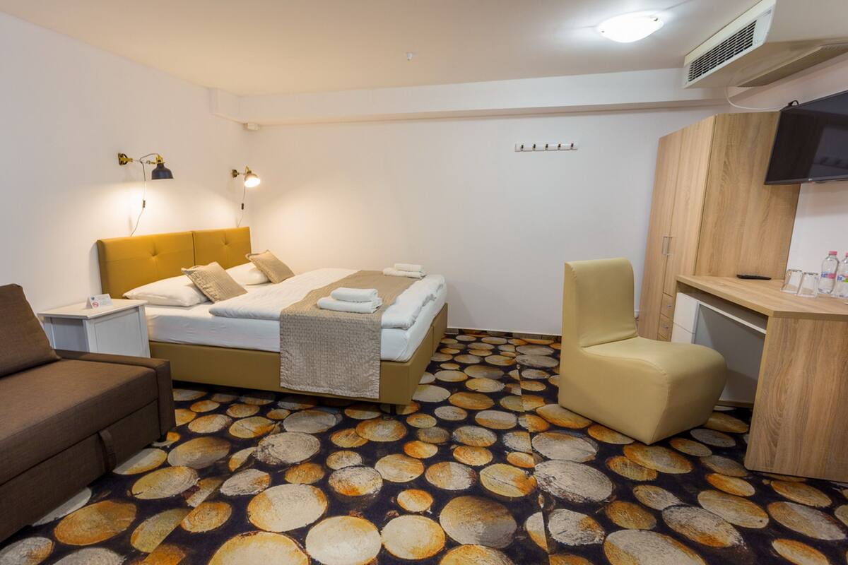 A hotel room with a bed, a sofa, a chair, a desk, and a television.