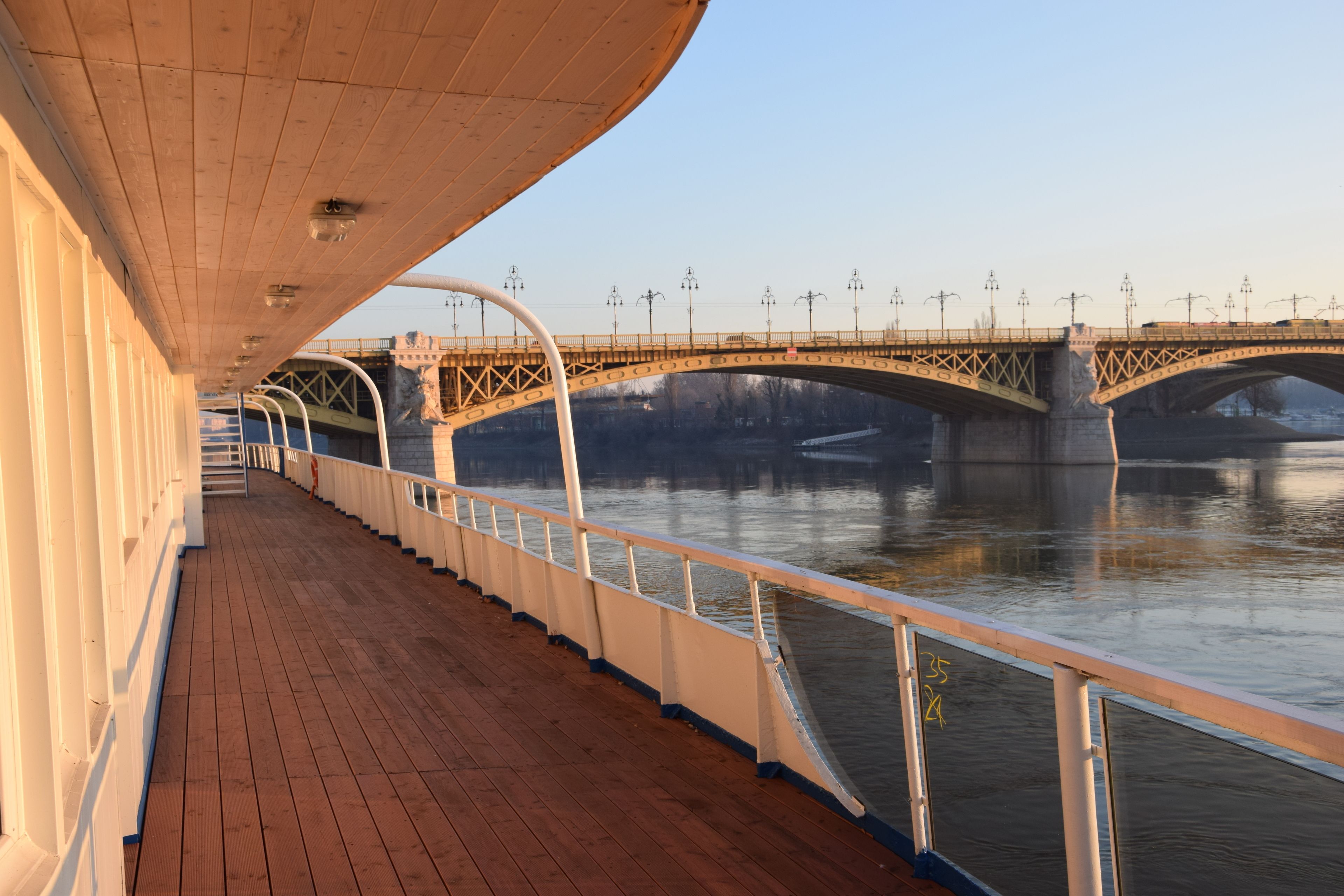 A deck with a railing overlooking a river and a bridge.
