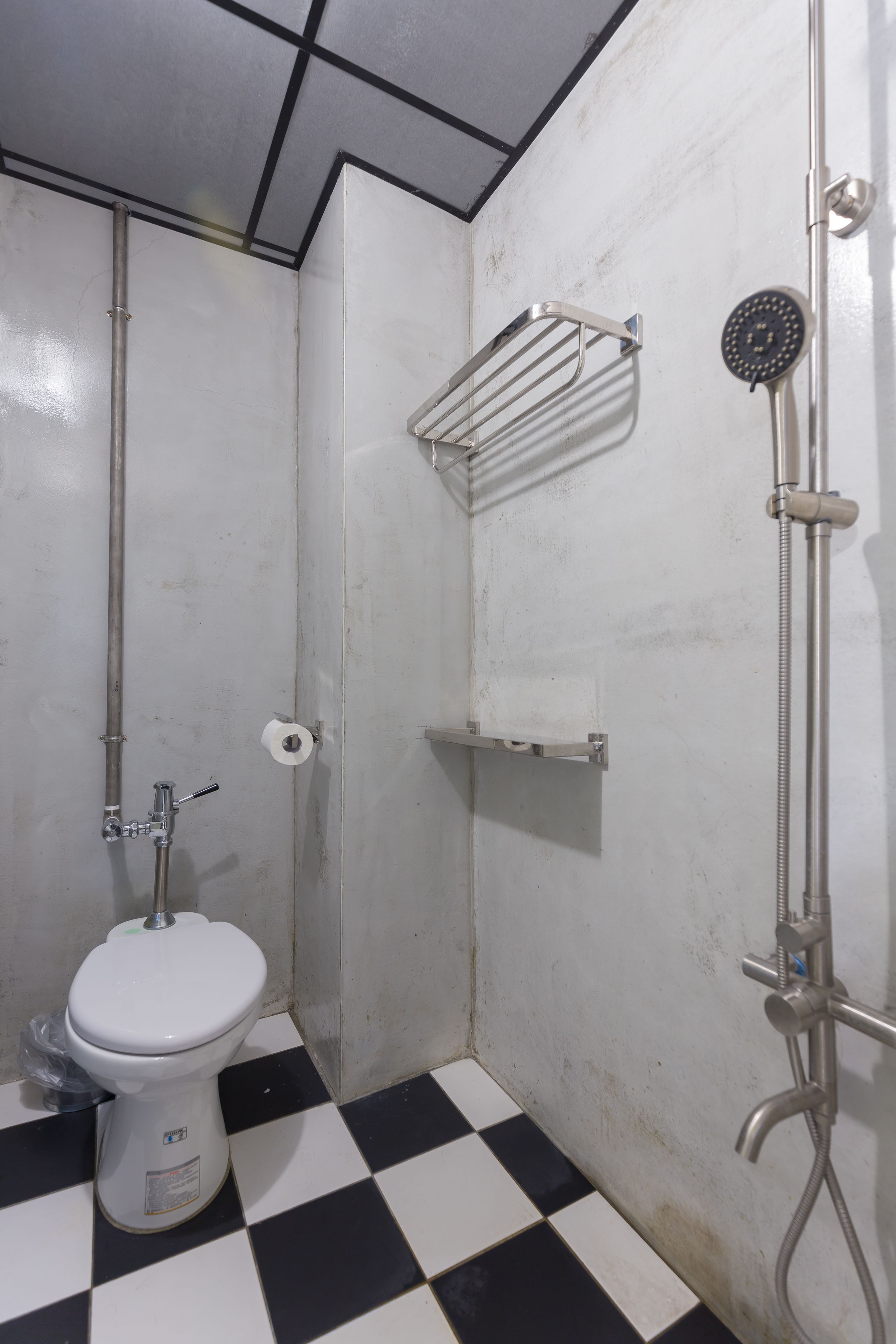 A small, tiled bathroom with a toilet, a shower, and a metal shelf.