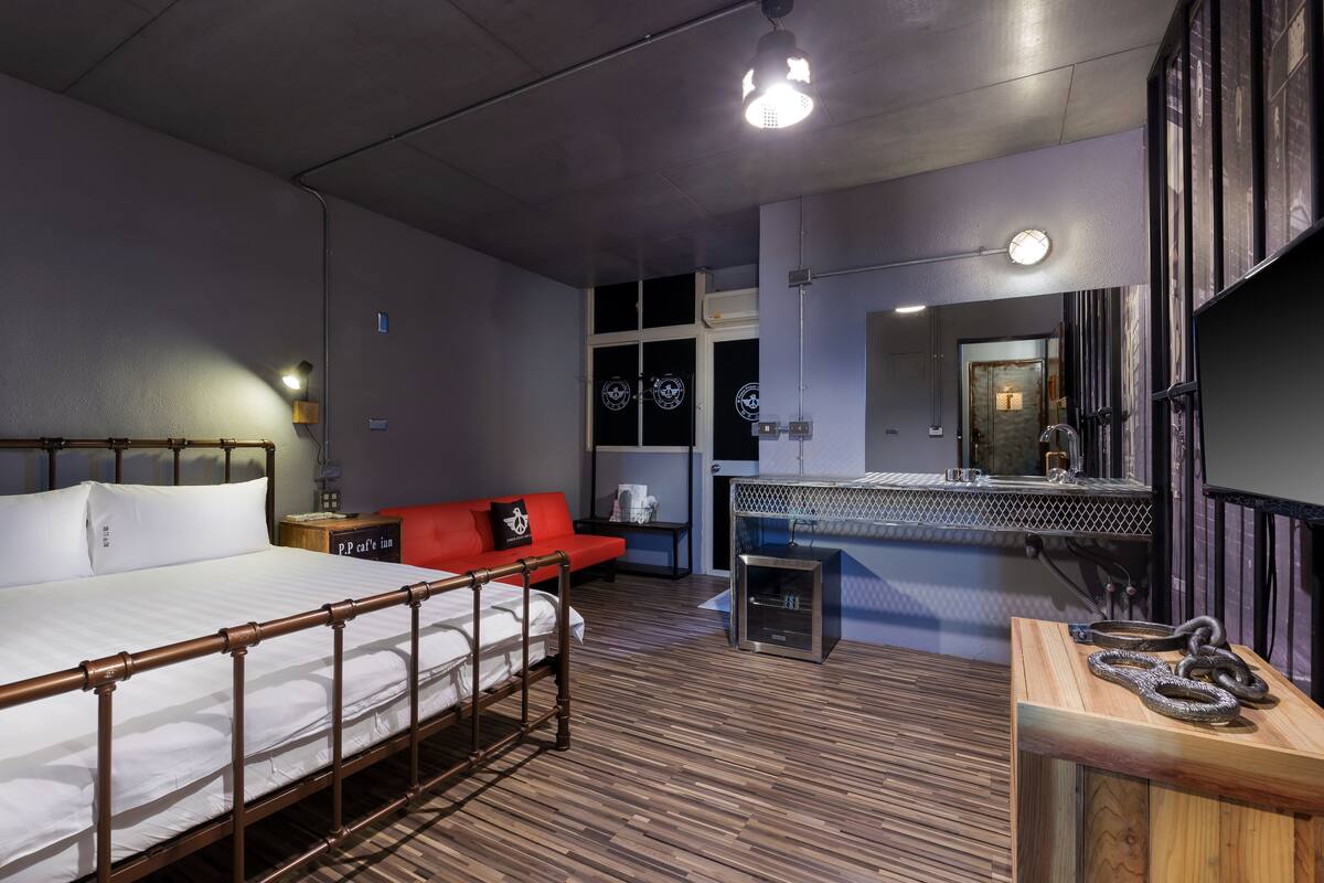 A modern hotel room with a large bed, a red sofa, a small desk, and a mirror.