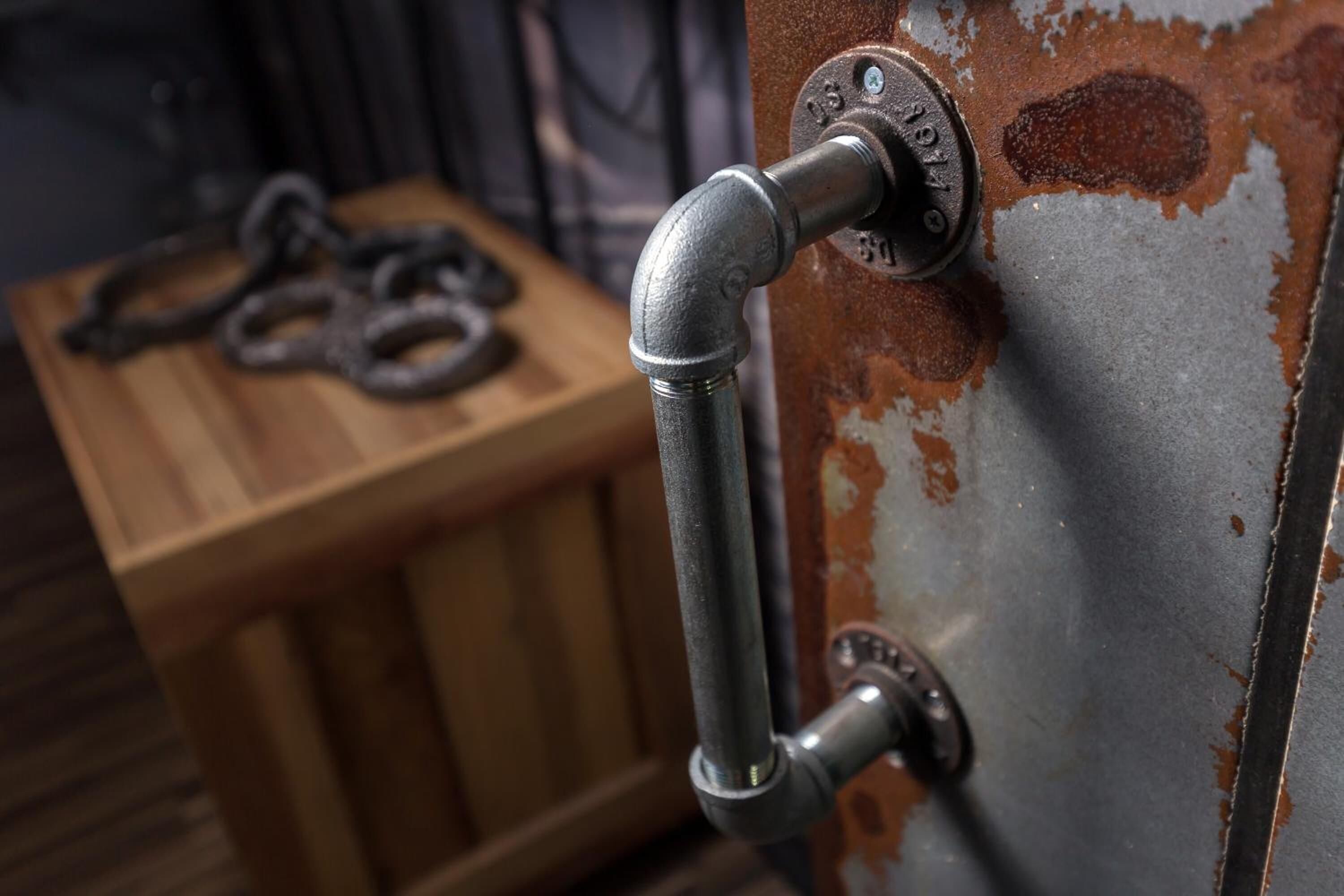 A metal pipe attached to a rusted metal surface, with a wooden crate in the background.