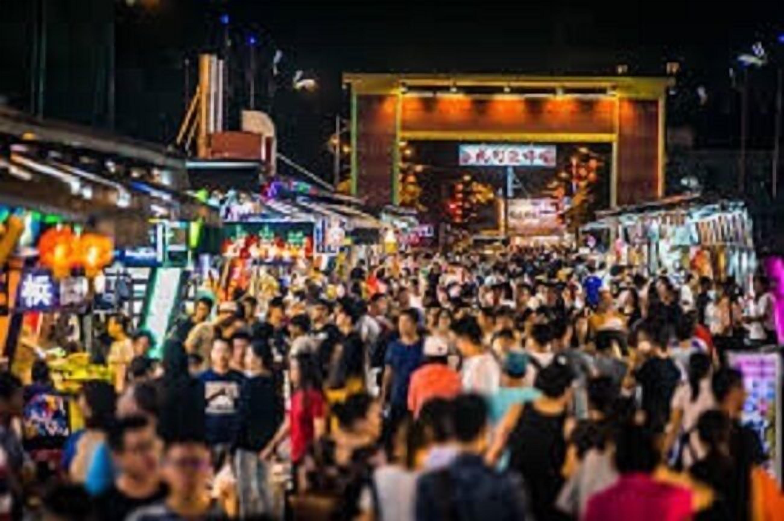 A crowded street scene with various shops and signs, indicating a busy urban area.