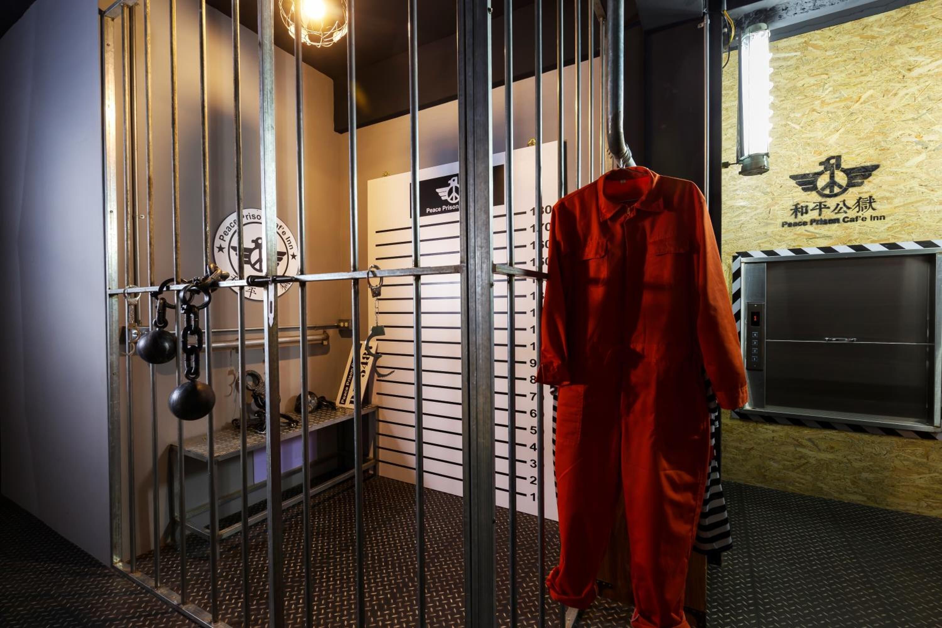 A metal gate with a height chart, a red jumpsuit hanging on the gate, and a sign with a peace symbol and text.