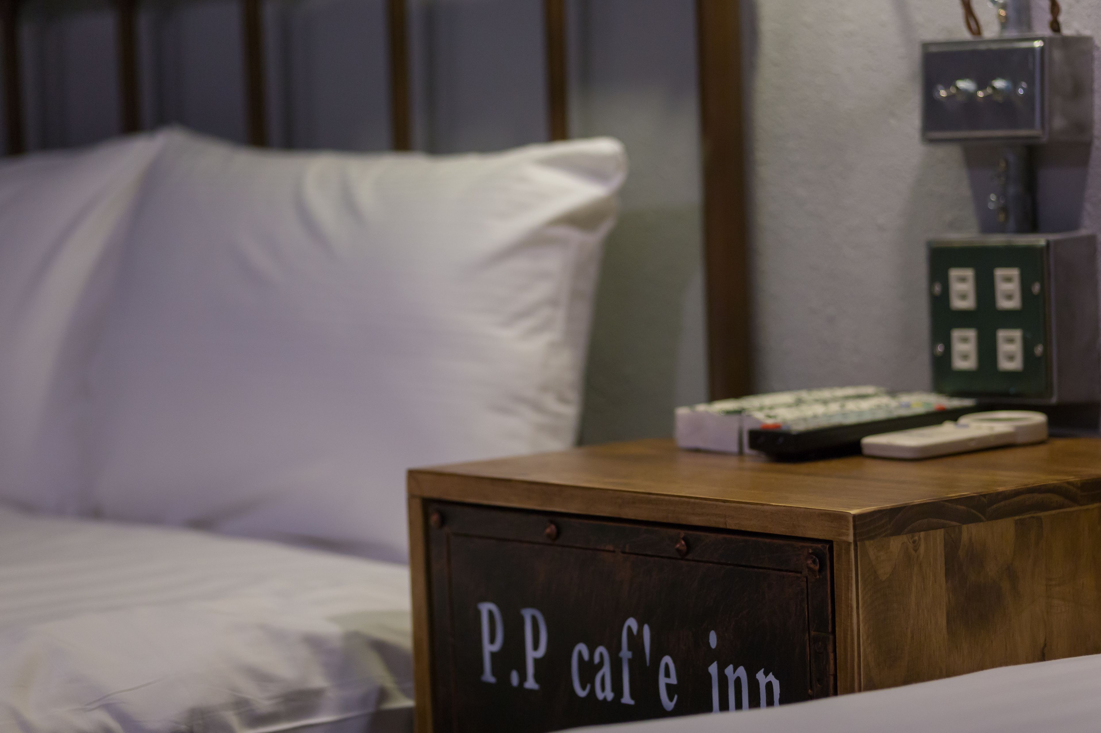 A bed with white bedding and a sign on a wooden nightstand that reads "P.P cafe inn".