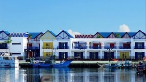 A row of colorful buildings with balconies, a marina with boats, and a clear blue sky.