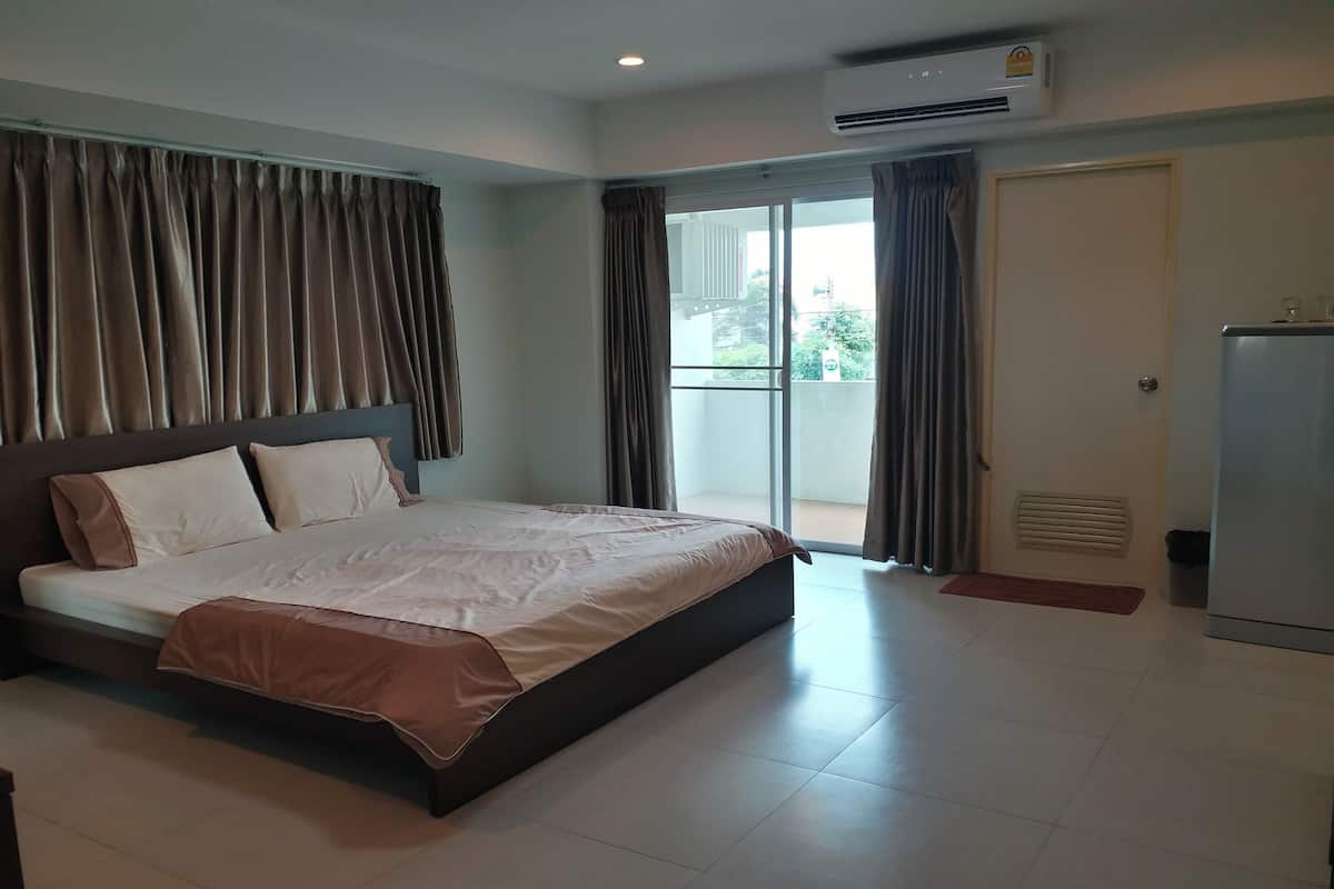 A hotel room with a bed, a sliding glass door to the outside, an air conditioning unit, and a refrigerator.