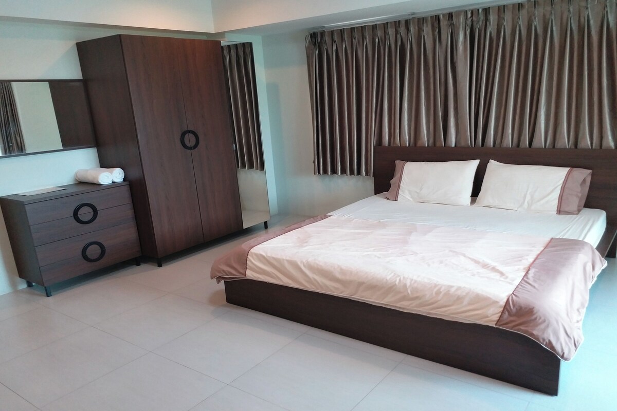 A bedroom with a bed, a wardrobe, a dresser, and a large window with curtains.