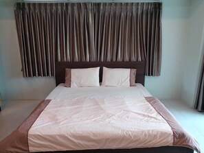 A neatly made bed with a headboard, a plain wall, and a window with curtains. - TongPrasit Place (Nakhon Ratchasima)