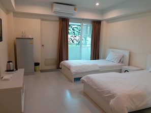 A hotel room with two beds, a desk, a refrigerator, and a window with curtains. - TongPrasit Place (Nakhon Ratchasima)