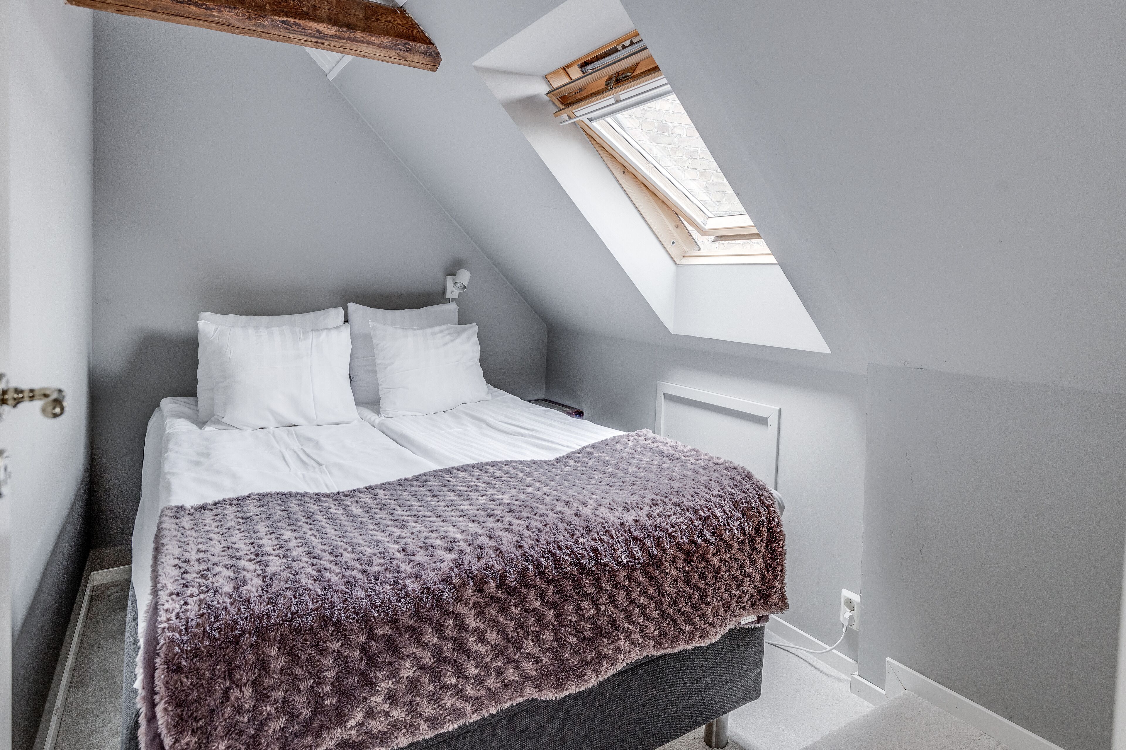 Un dormitorio con cama, ventana y tragaluz.