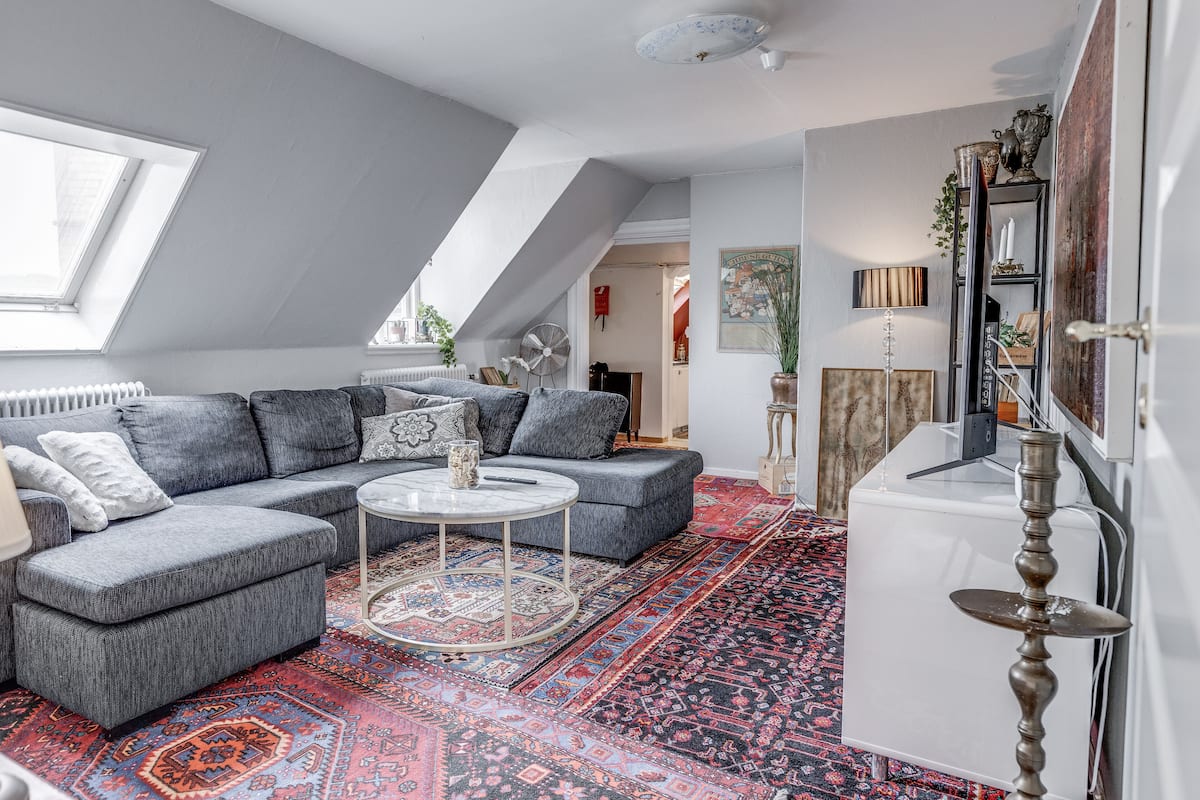 Un appartement moderne de style « loft » avec un canapé d’angle gris, une table basse ronde et un tapis à motifs.