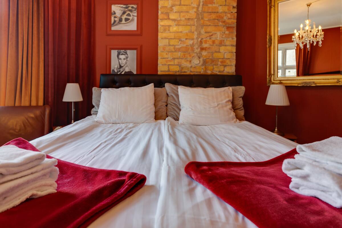 Une chambre d’hôtel avec un grand lit, des rideaux rouges, un mur en briques et un lustre.