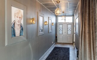 A hallway with framed pictures on the wall, a black rug, and a door with decorative glass panels.
