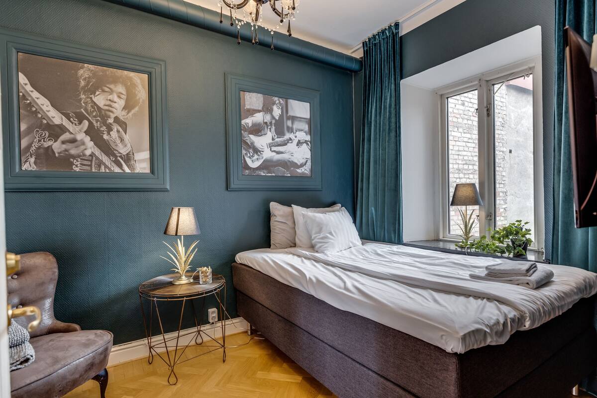 Une chambre à coucher avec un grand lit, une chaise, une petite table avec une lampe et des tableaux encadrés accrochés au mur.