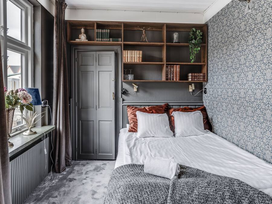 A bedroom with a bed, a window, a bookshelf, and a door.
