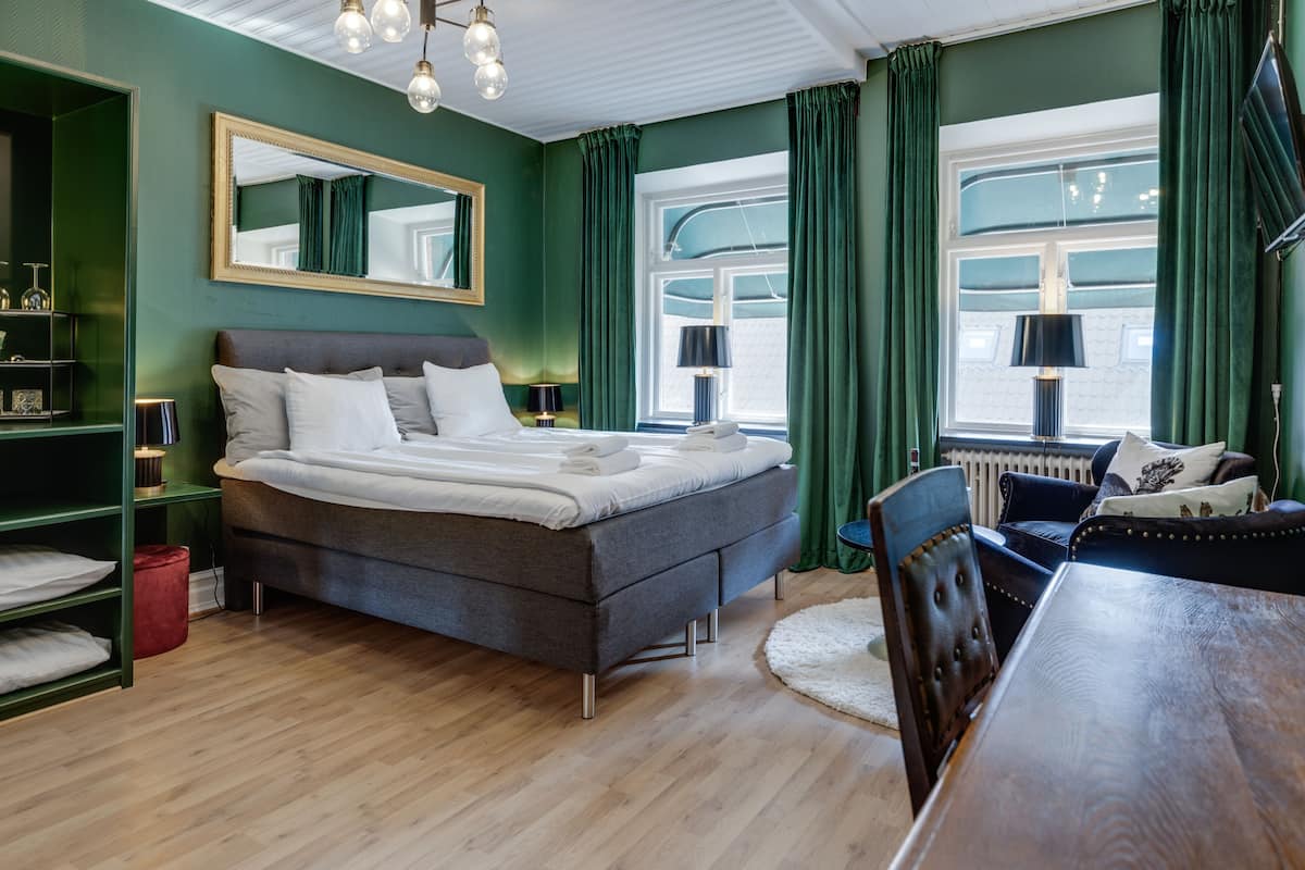 Une chambre à coucher avec un lit, une commode, une chaise, une table et une fenêtre avec des rideaux.