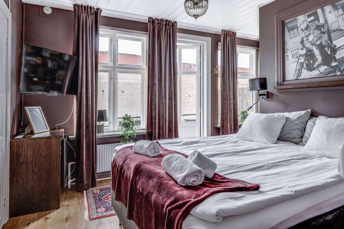 Une chambre d’hôtel avec un grand lit, un téléviseur à écran plat, un bureau avec un ordinateur et une fenêtre avec des rideaux.