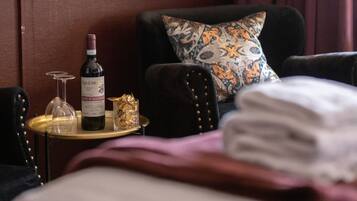 Habitación de hotel con cama, mesita de noche, una botella de vino, una copa y un objeto decorativo.