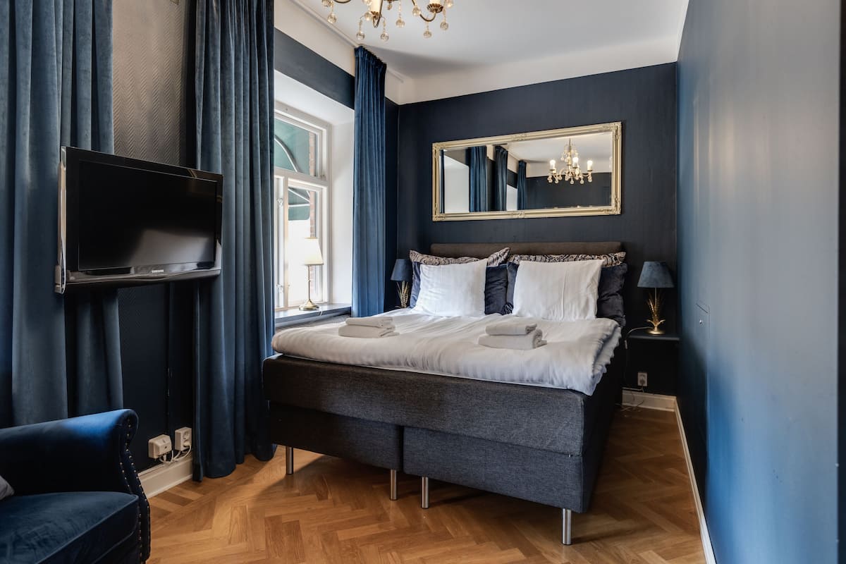 Une chambre à coucher comprenant un lit, un téléviseur fixé au mur, une table de chevet et un miroir.