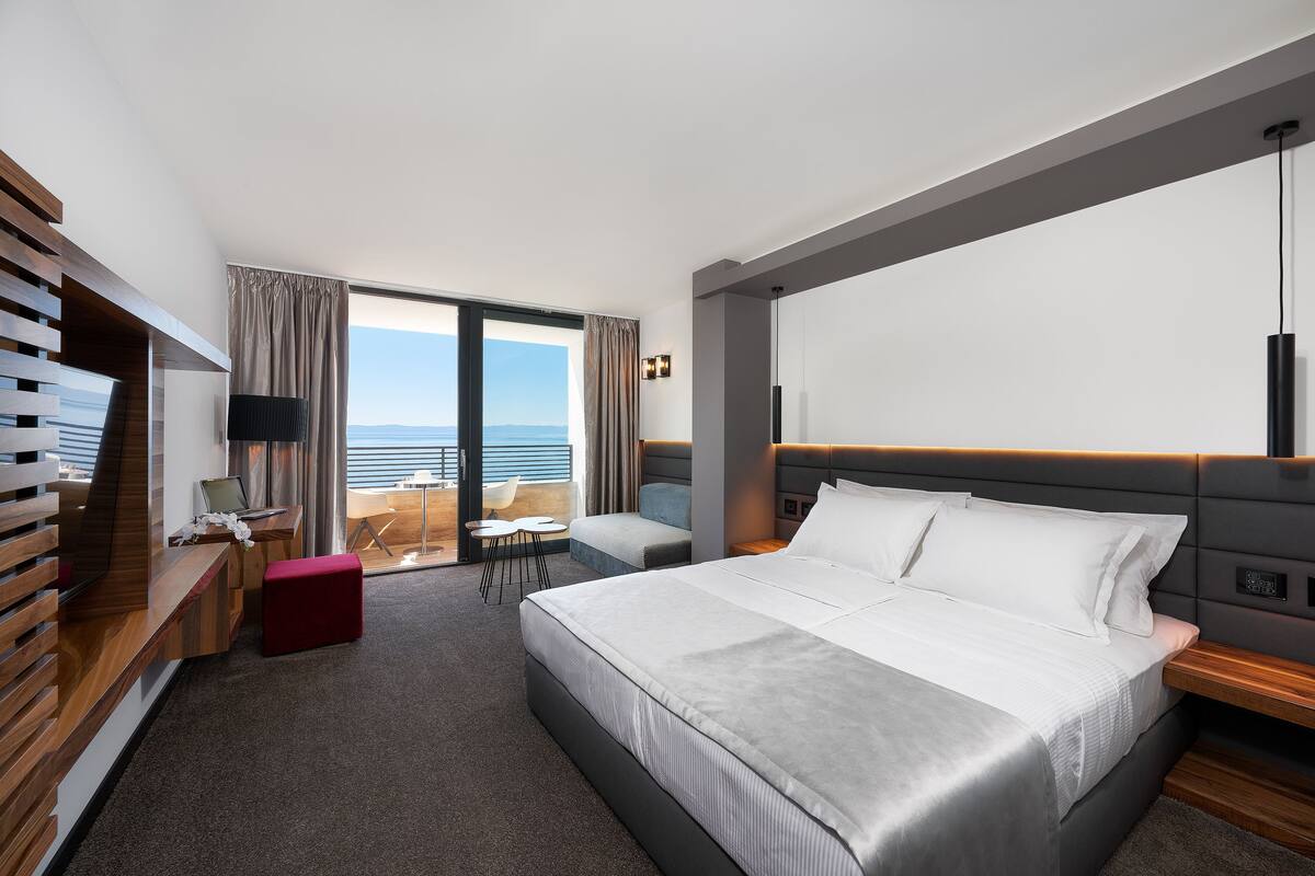 A modern hotel room with a large bed, a desk, a chair, and a view of the ocean.