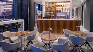 A modern bar area with a wooden counter, various liquor bottles, and a seating area with white chairs and round tables. - Hotel Ani (Makarska)