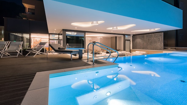 A modern indoor swimming pool with clear water, surrounded by lounge chairs and a sun terrace. - Hotel Ani (Makarska)